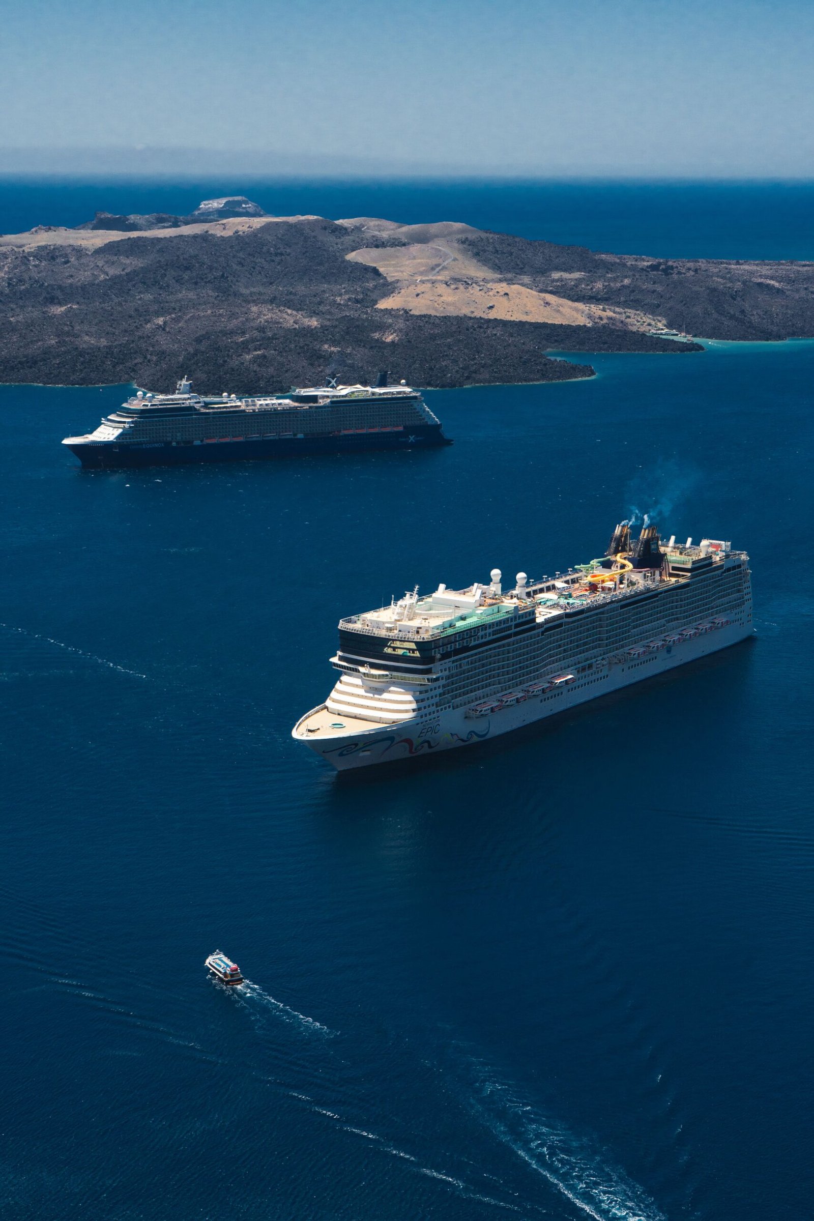 Aerial view of luxury cruise ships near Fira, Greece, showing the vibrant blue Aegean Sea.